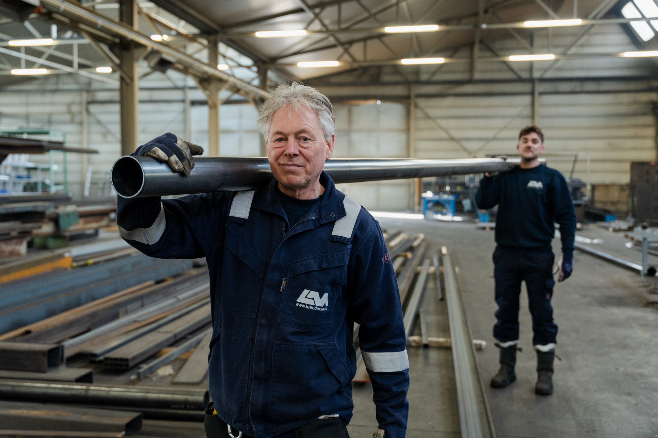 Twee medewerkers dragen een metalen pijp op hun schouder.